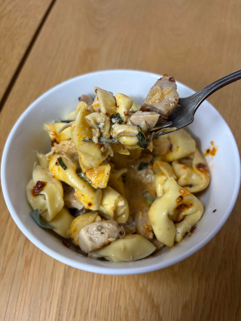 Brown butter sage tortellini with seared chicken, topped with chili crisp and shaved Parmesan